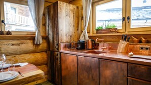 Une cuisine rustique dans un chalet, avec des murs en bois, un évier en cuivre et un coin repas avec une table mise pour deux personnes.