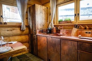 Une cuisine rustique dans un chalet, avec des murs en bois, un évier en cuivre et un coin repas comprenant une table et des chaises en bois.
