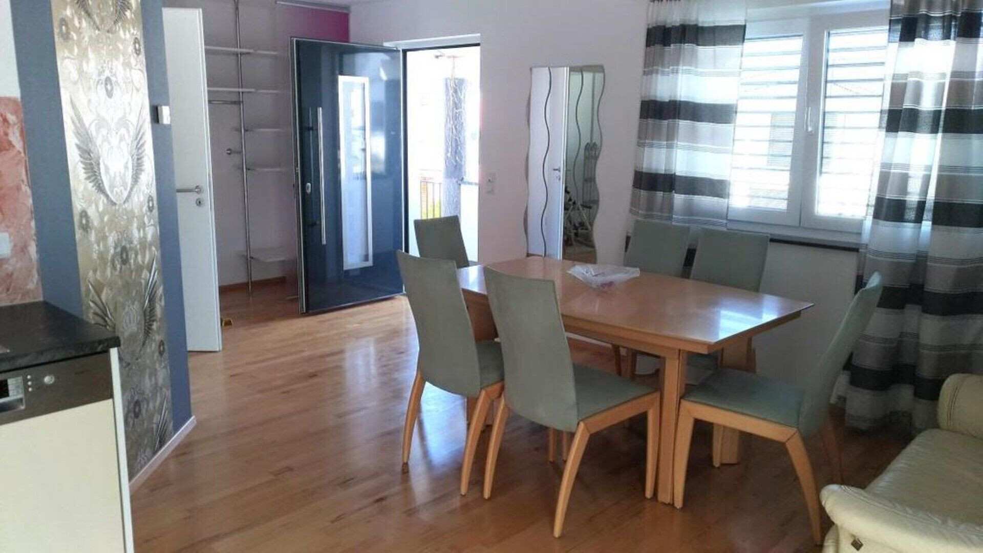 Ein Essbereich mit Holztisch und -stühlen, eine Küchenzeile mit Kühlschrank und eine Tür zu einem anderen Raum.