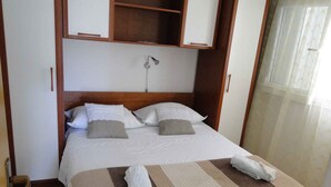 Un lit bien fait, avec une couvre-lit à rayures, deux oreillers et une serviette roulée posée sur une table de chevet, dans une chambre d'hôtel.