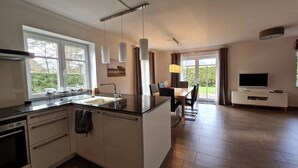 Une cuisine moderne dotée d’un îlot central, d’un coin repas avec une table et des chaises, d’un téléviseur et d’une grande fenêtre offrant une vue sur l’extérieur.