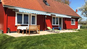 A red house with a tiled roof, a porch with a table and chairs, and a small garden area. - Wood-semidetached house, ideal for 2 families (Brodersby)