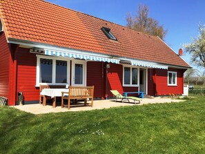 Ein rotes Haus mit einem Ziegeldach, einer Veranda mit Tisch und Stühlen sowie einem kleinen Garten.