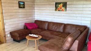 A brown leather sectional sofa with a wooden coffee table in a room with wooden walls and a wooden floor. - Wood-semidetached house, ideal for 2 families (Brodersby)