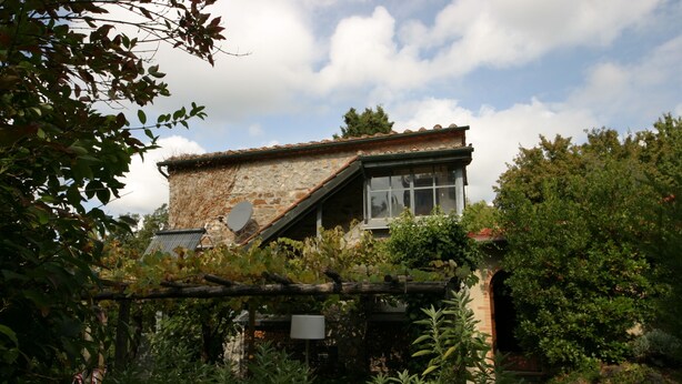 Ein rustikales Steinhaus mit geneigtem Dach, großen Fenstern und einer Satellitenschüssel.