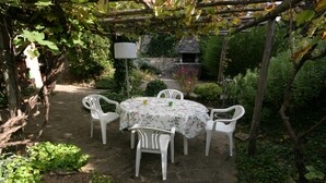 Ein Garten-Terrasse mit rundem Tisch und vier Stühlen, umgeben von Grünpflanzen und einer Pergola.