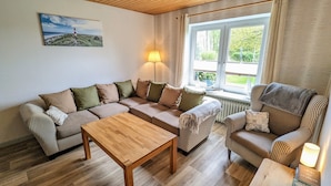 Ein gemütliches Wohnzimmer mit einer Eckcouch, einem Holztisch und einem Fenster mit Vorhängen.