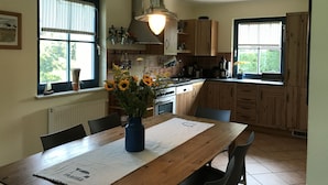 Une cuisine avec des meubles de rangement en bois, une table à manger avec des chaises et un vase rempli de tournesols.
