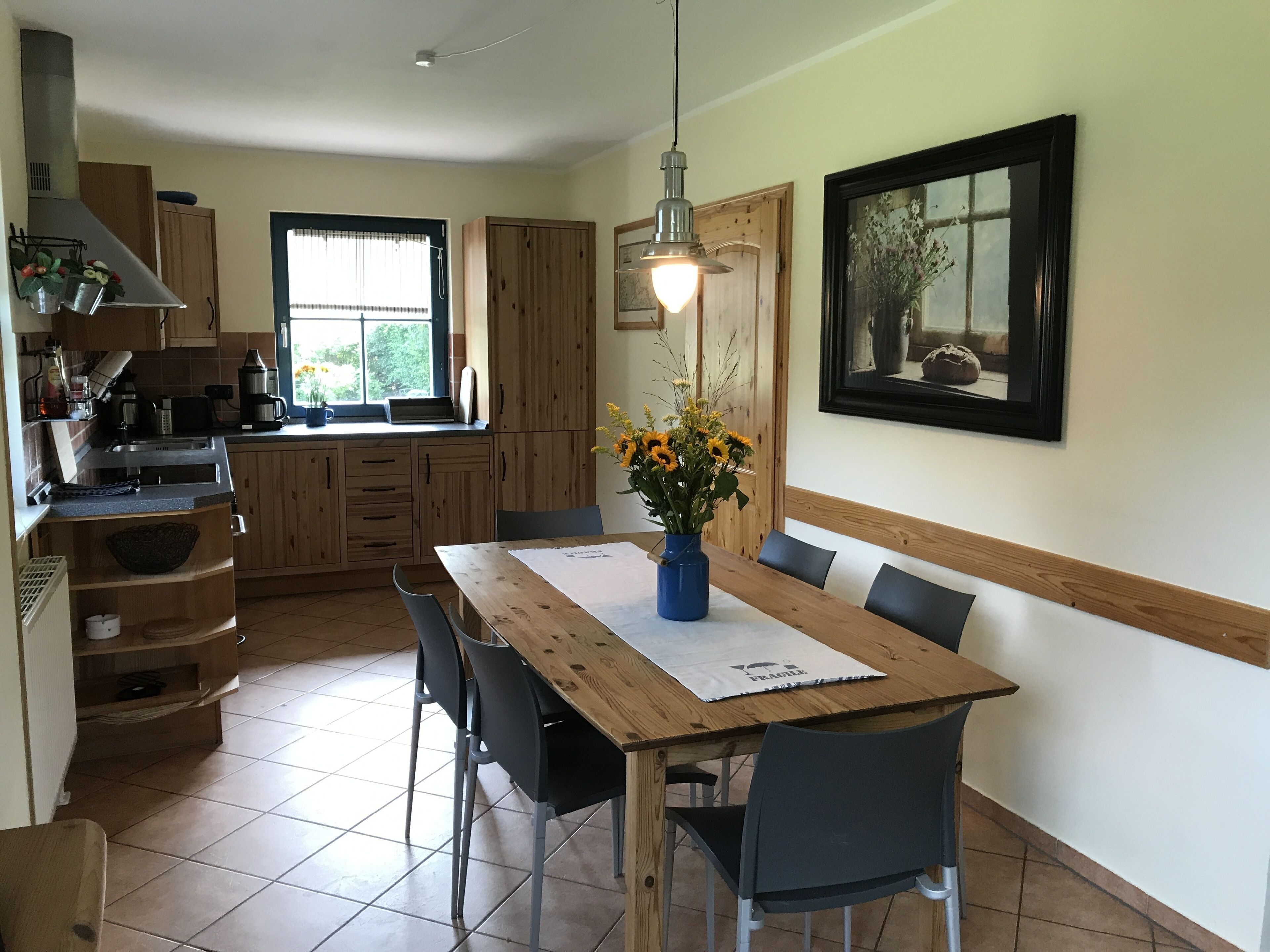 Eine Küche mit Holzausstattung, einem Esstisch mit Stühlen, einer Vase mit Blumen und einem gerahmten Bild an der Wand.