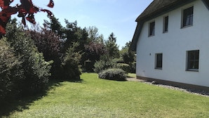 Un bâtiment blanc avec un toit de chaume, entouré d’une pelouse bien entretenue et de divers arbustes.