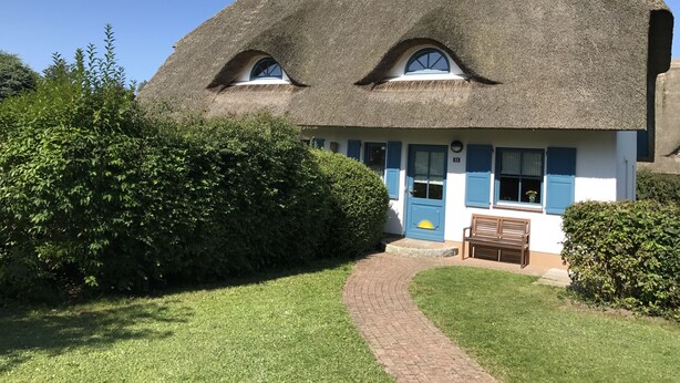 Une maison traditionnelle avec un toit de chaume, un porche et un petit jardin.