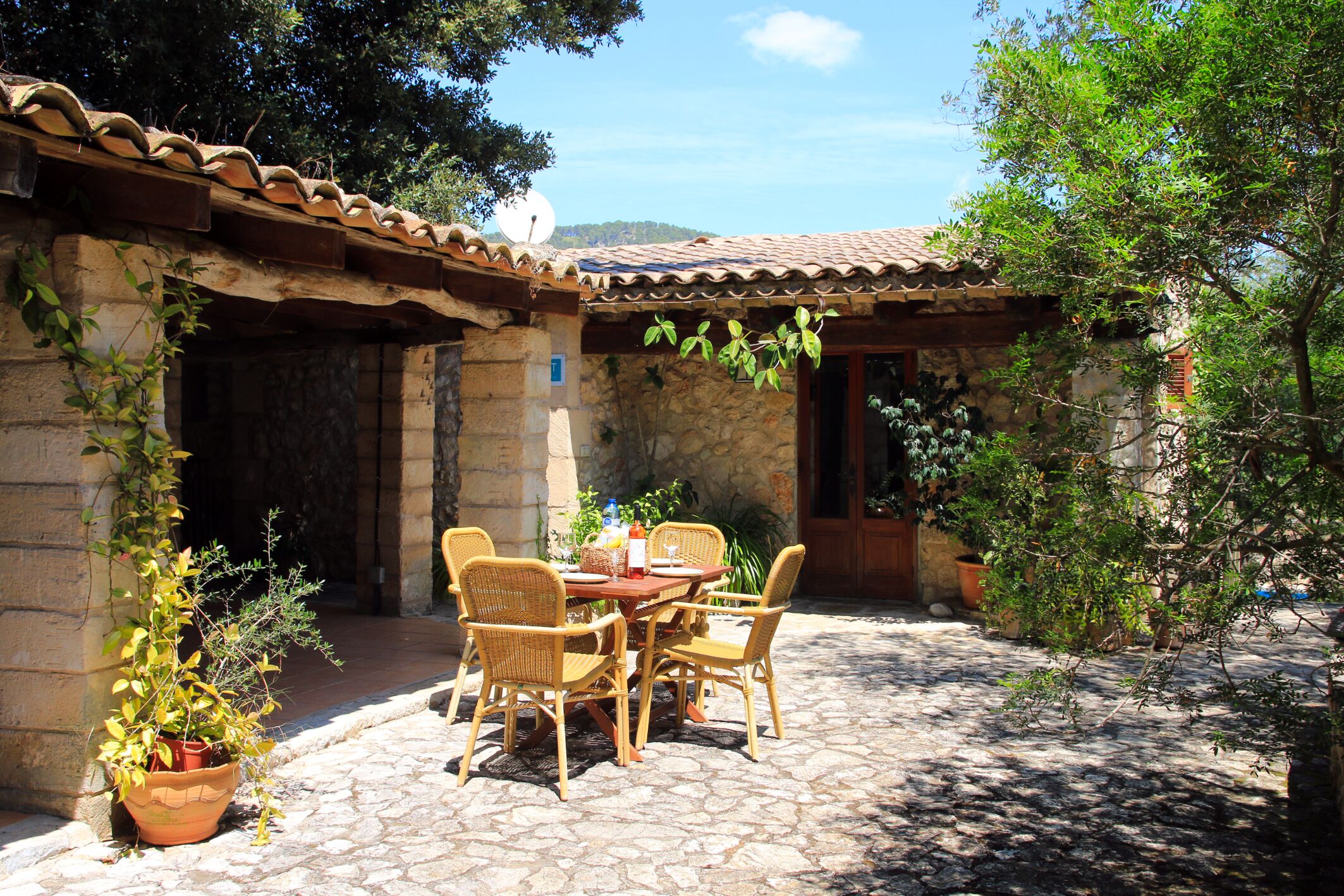 Un bâtiment en pierre avec un toit en tuiles, une cour intérieure avec une table et des chaises, et des plantes en pot.