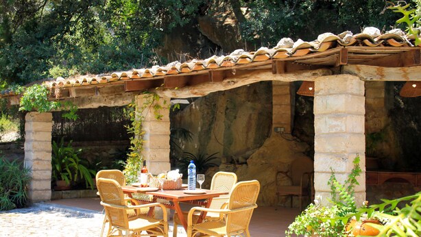 An outdoor patio with a stone table and wicker chairs, surrounded by potted plants and a stone wall. - Rural tranquillity at the foot of the Tramuntana, pool with panoramic views (Campanet)