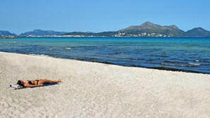 A beach with a person sunbathing, clear blue water, and distant mountains. - Rural tranquillity at the foot of the Tramuntana, pool with panoramic views (Campanet)