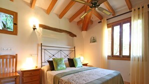 A bedroom with a wooden headboard, a bed with green and brown bedding, a nightstand with a lamp, a wooden chair, and a window with curtains. - Rural tranquillity at the foot of the Tramuntana, pool with panoramic views (Campanet)