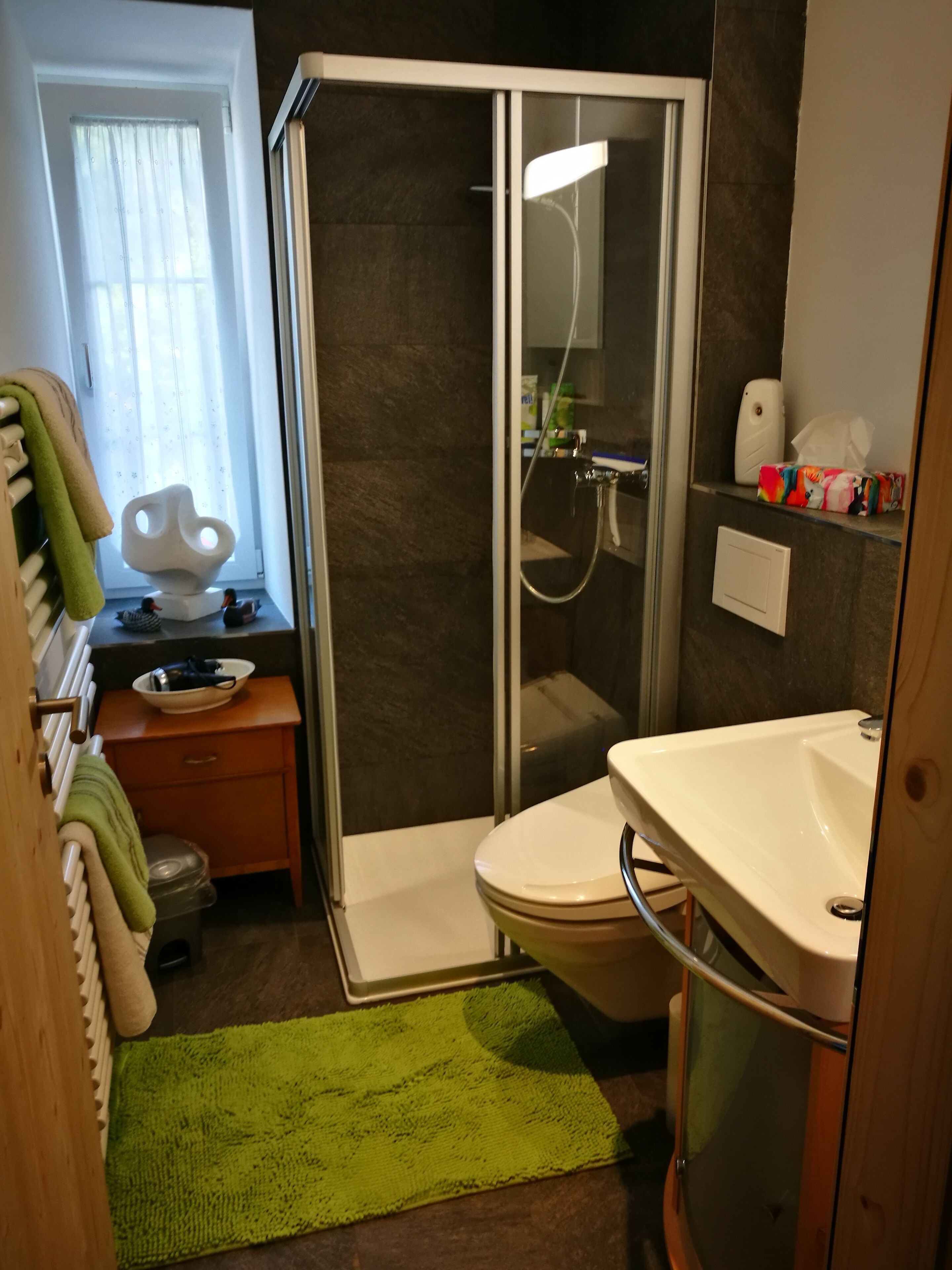 A bathroom with a glass-enclosed shower, a toilet, a sink, and a small vanity with a bowl.