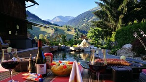 Une table dressée avec une vue imprenable sur les montagnes, une bouteille de vin, un saladier de fruits et un barbecue.