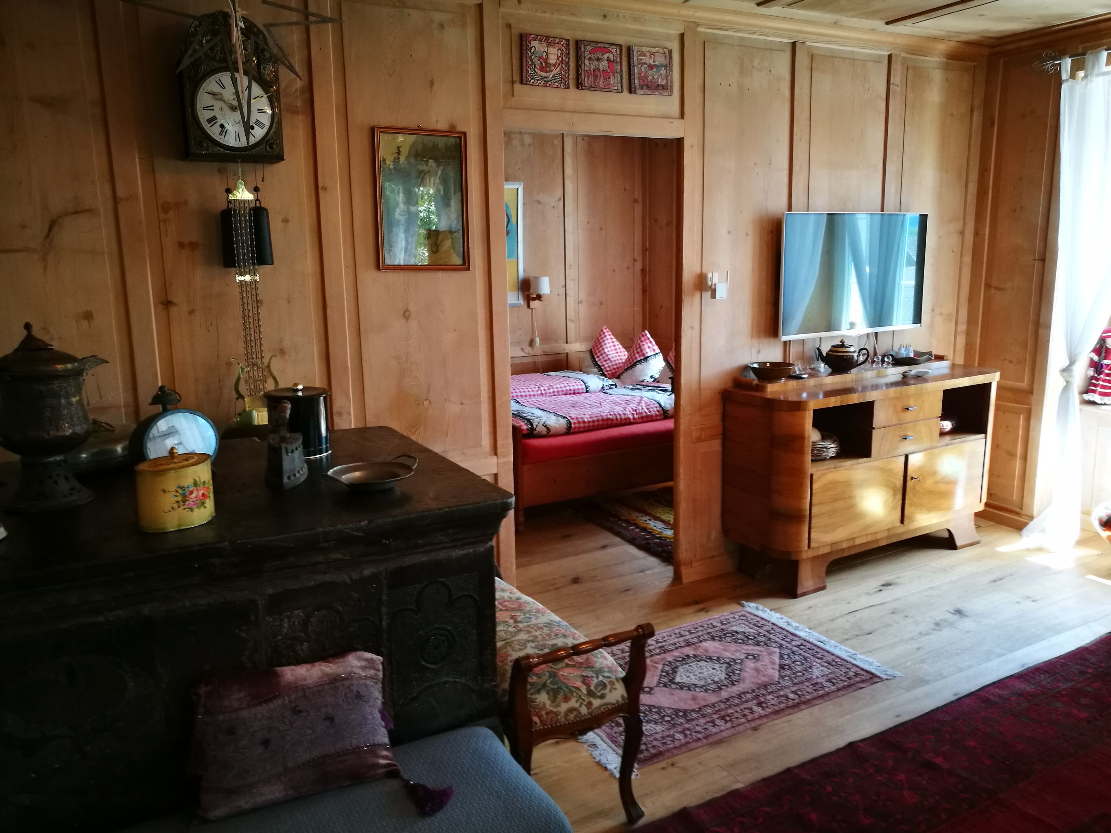Un interior de madera con una cama, un televisor, un armario de madera y un reloj.