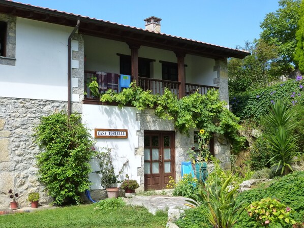 A two-story building with a stone base and a white upper section. There is a balcony with wooden railings and a sign reading "CASA TORIELLU".