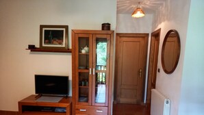 A living room with a TV, wooden cabinet, and a door leading to another room. - Apartment in Asturian country house, close to beach (Asturien)