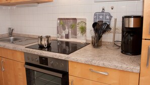A kitchen with wooden cabinets, a stainless steel sink, a coffee maker, and a stove. - Your little break at the North Sea: modern furnished apartment with living area (Carolinensiel)