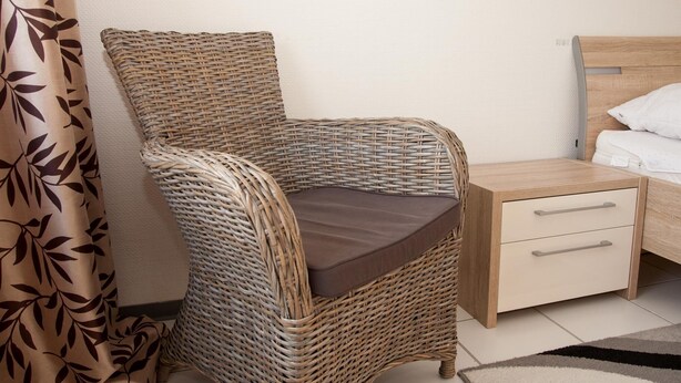 A wicker chair with a brown cushion, a wooden nightstand with drawers, and a bed with white bedding. - Your little break at the North Sea: modern furnished apartment with living area (Carolinensiel)