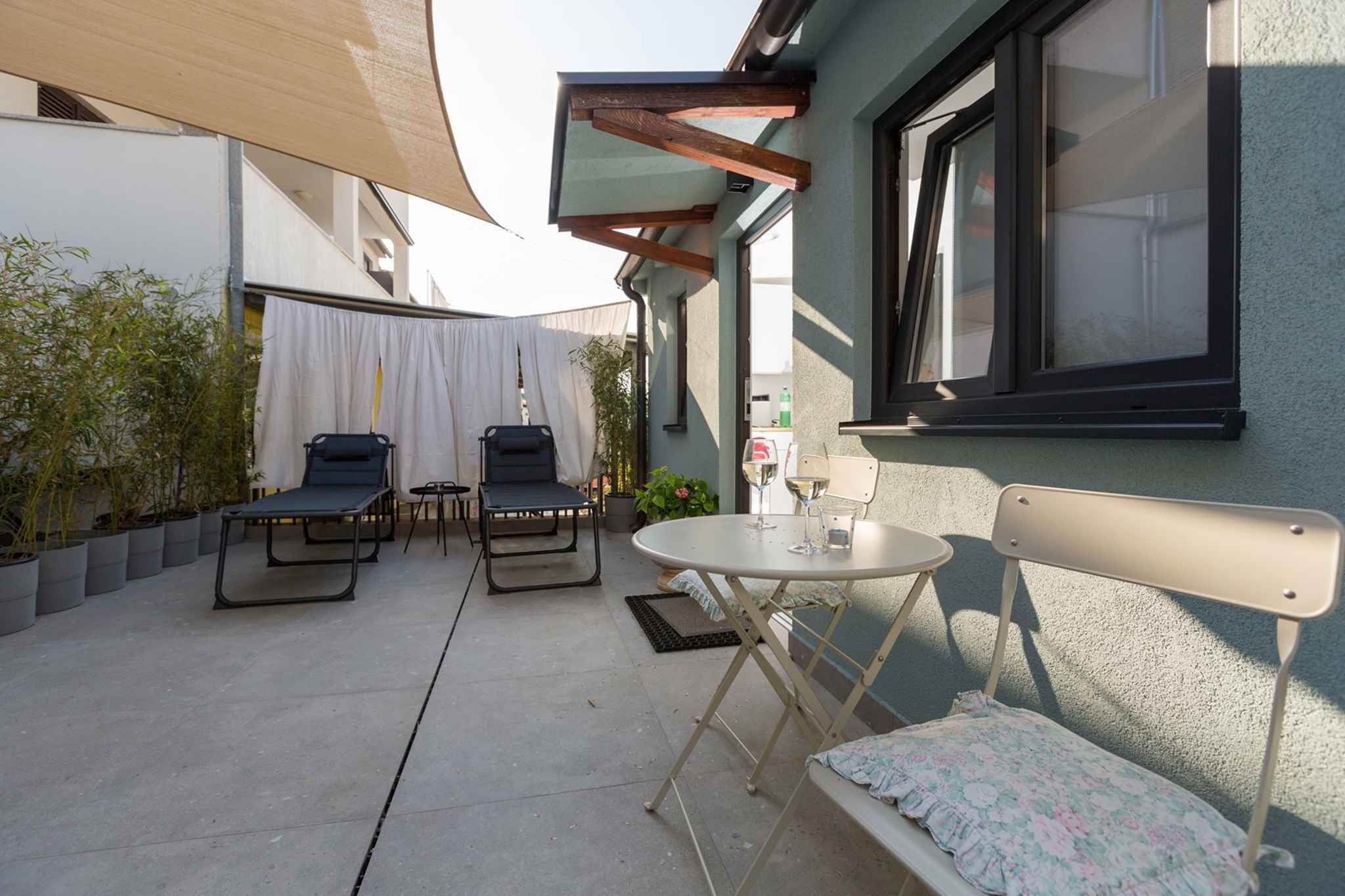 Eine Terrasse mit Tisch, zwei Stühlen, einer Bank und Kübelpflanzen.