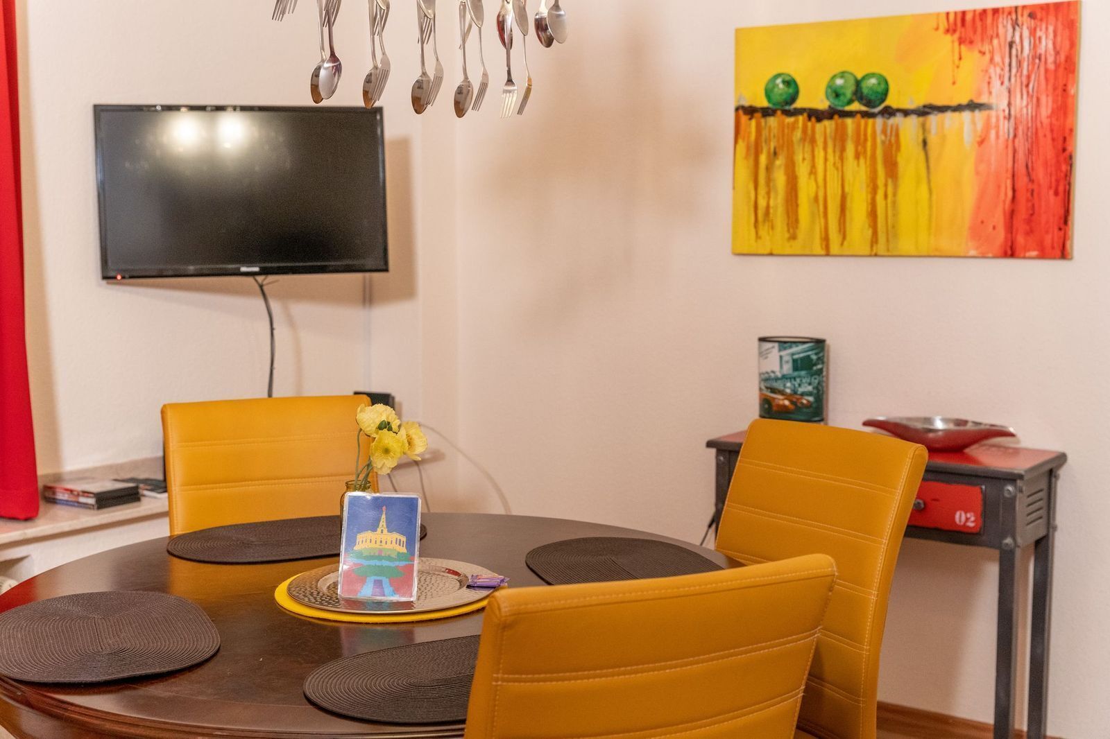A dining area with a round table, two yellow chairs, a vase with yellow flowers, and a painting on the wall.