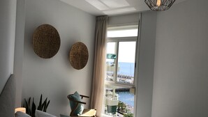 A bedroom with a bed, a chair, a window with a view of the sea, and two wall-mounted circular decorations. - Right on the beach quiet apartment with a large terrace (Radazul)