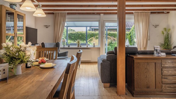 A modern kitchen with wooden cabinets, a dining table, and a sofa. There are large windows with curtains, a plant, and a view of greenery outside. - Roof top house with 3 bedrooms in Carolinensiel (90 m²) for 6-7 persons (Carolinensiel)