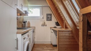 A compact kitchen with a washing machine, wooden cabinets, and a window. - Roof top house with 3 bedrooms in Carolinensiel (90 m²) for 6-7 persons (Carolinensiel)