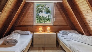 A cozy attic bedroom with two beds, a small window with a view of trees, and a wooden ceiling. - Roof top house with 3 bedrooms in Carolinensiel (90 m²) for 6-7 persons (Carolinensiel)
