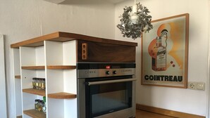 A compact kitchen with a built-in oven, wooden shelves, and a hanging light fixture. - Apartment with a beautiful mountain view (Garmisch-Partenkirchen)