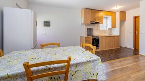 Eine kleine Küche mit Holdekor-Schränken und einem Herd, ein Essbereich mit Tisch und Stühlen sowie ein weißes Kühlschrank.
