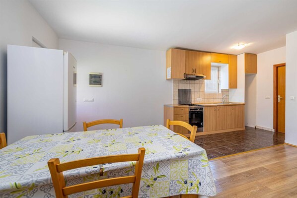 A compact kitchen with wooden cabinets and a stove, a dining area with a table and chairs, and a white refrigerator.