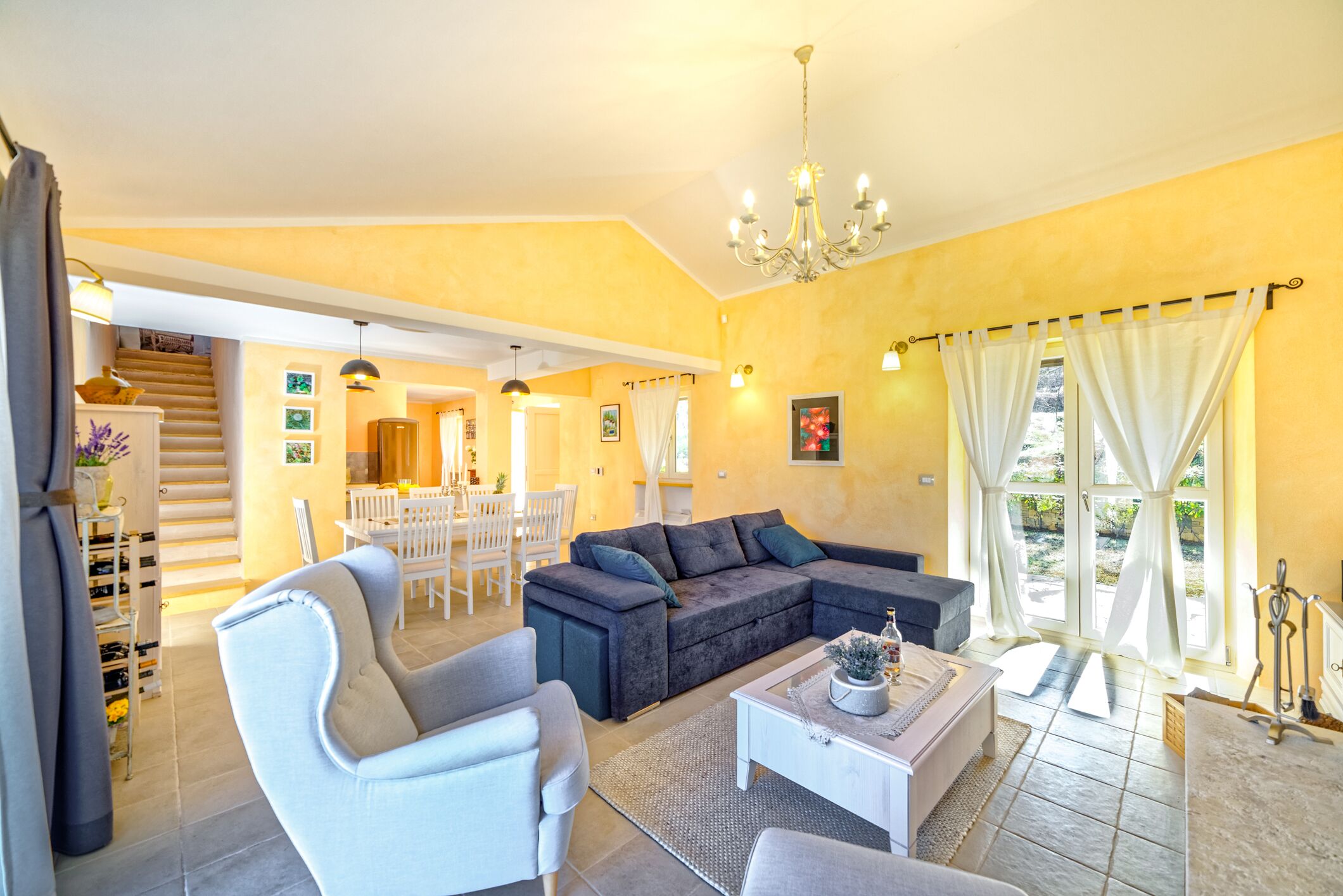 A spacious living area with a dark-colored sofa, a white armchair, and a coffee table. A staircase leads to a dining area with a white table and chairs.