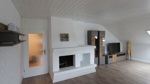 A modern living room with a white brick fireplace, a television on a wooden stand, and a wooden floor. - modern, very spacious apartment in the immediate vicinity of the Center Parcs (Medebach)