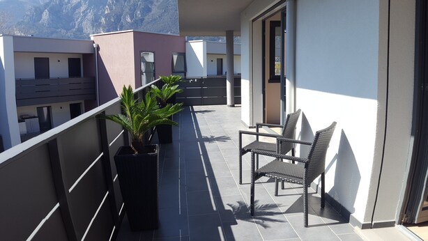 A balcony with a potted plant, two wicker chairs, and a view of mountains. - Nice vacation apartment in S. Alessandro-Riva del Garda. (riva del garda)