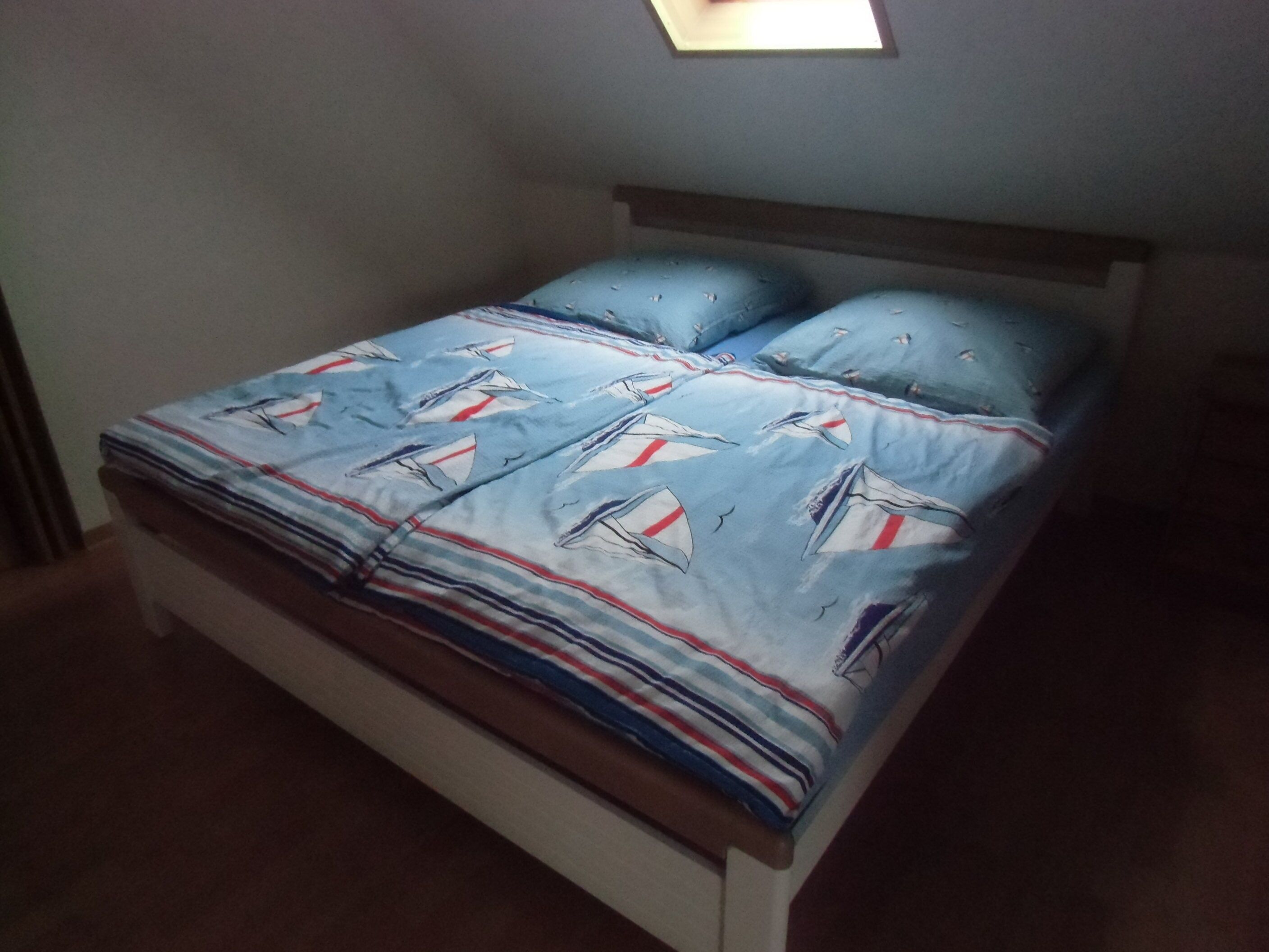 Ein Bett mit blau-weißem Segelbootmuster, zwei Kissen und ein Holz-Kopfbrett.