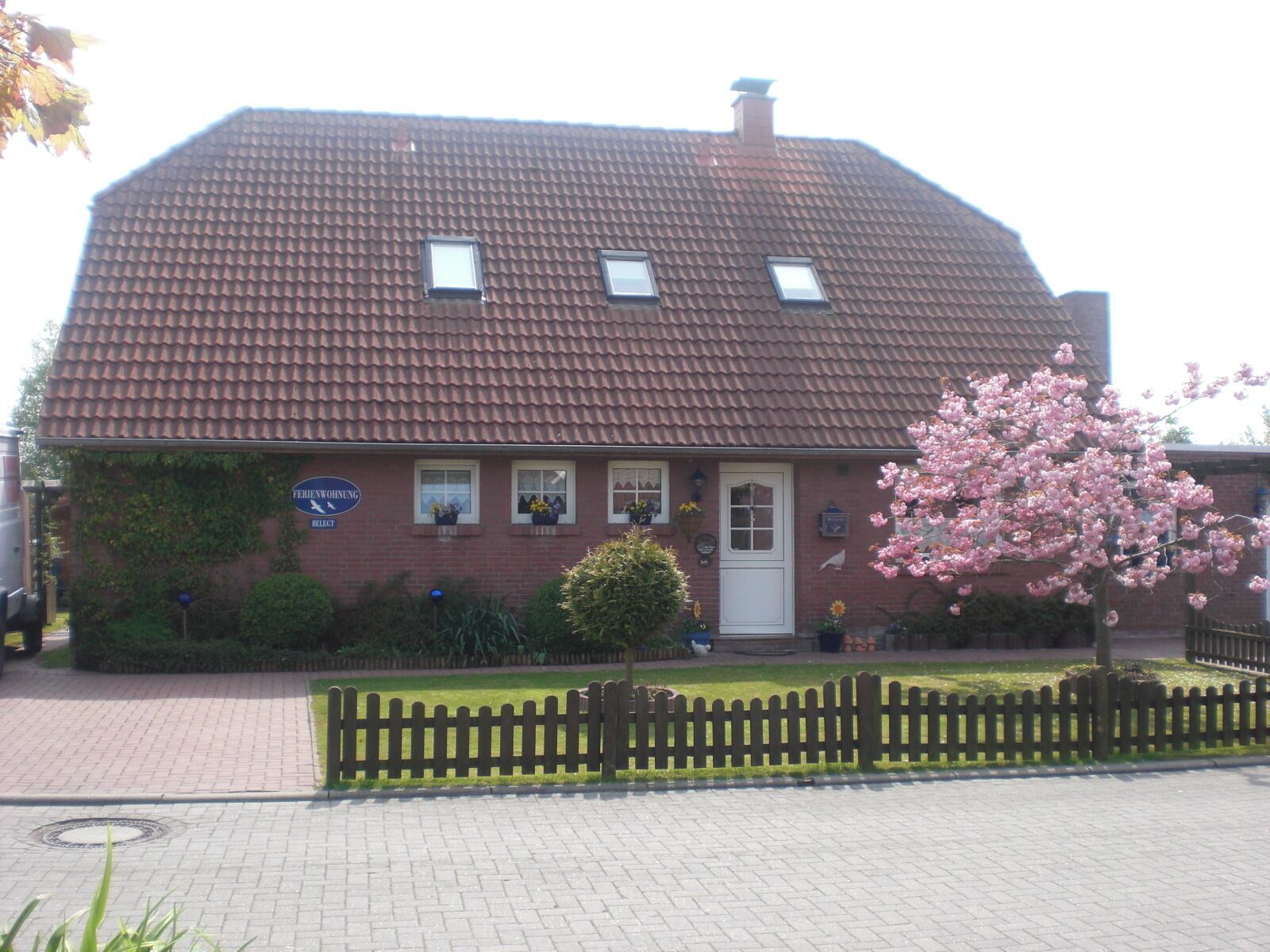A two-story building with a red-tiled roof, a small porch, and a sign indicating it is a residential property.