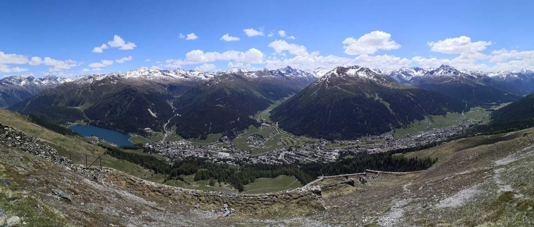 Een bergachtig landschap met een stadje in een vallei, omringd door besneeuwde bergtoppen.