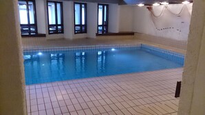 An indoor swimming pool with tiled floors and walls, large windows, and a tiled ceiling.