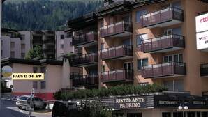 A multi-story hotel with balconies, a restaurant named "Ristorante Padrino," and a mountain backdrop.