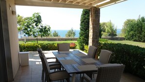 Eine Terrasse im Freien mit Tisch und Stühlen, einer Steinsäule und Blick aufs Meer.
