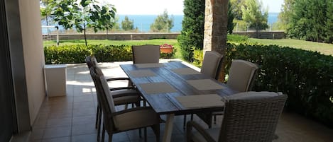 An outdoor patio with a table and chairs, a stone pillar, and a view of the sea.