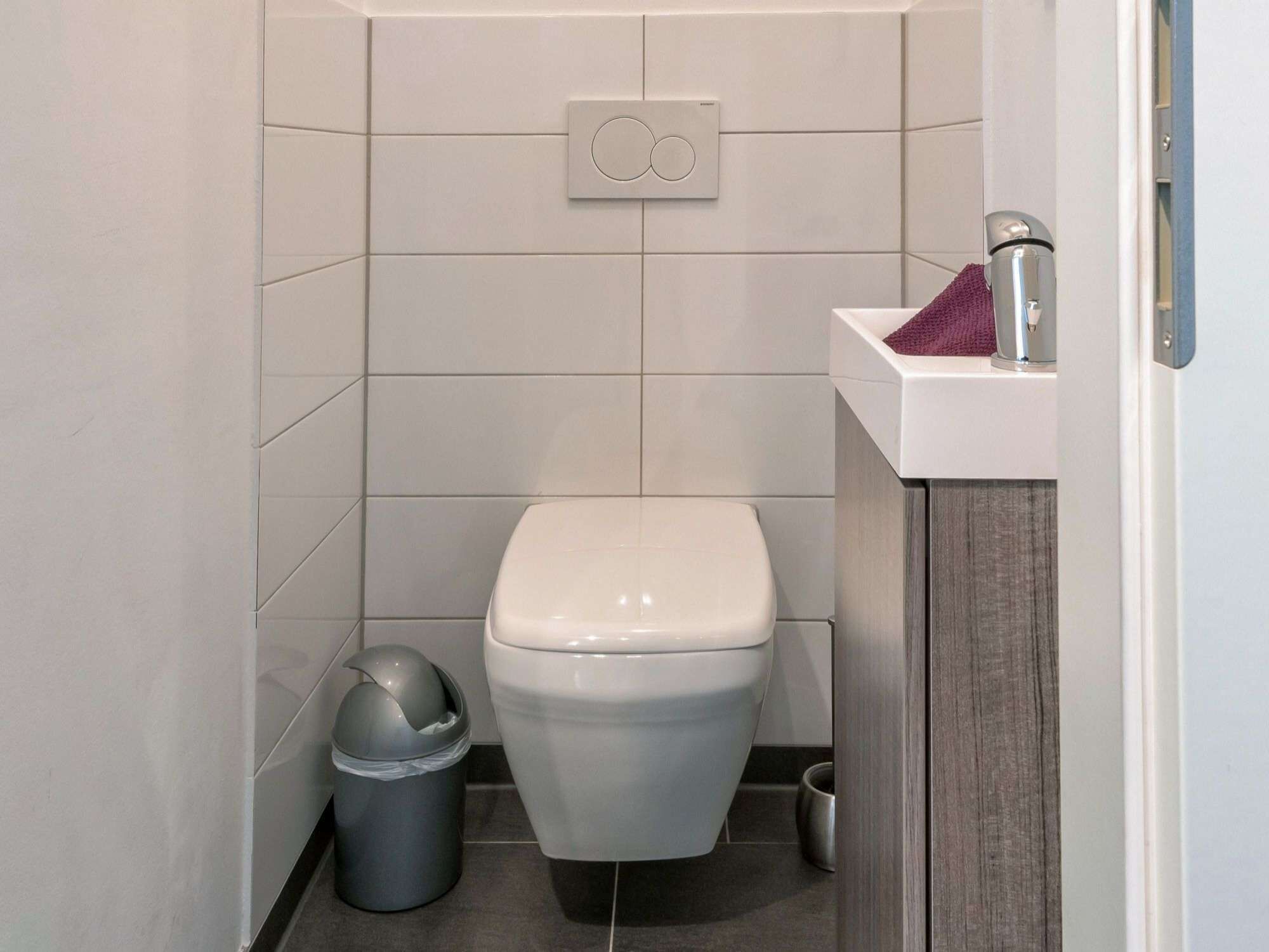 A small, modern bathroom with a toilet, a trash bin, and a sink with a towel.