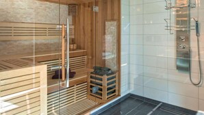 En moderne sauna med træbænke og et glasafsnit, samt et bruseområde med glasdør og flisegulv.