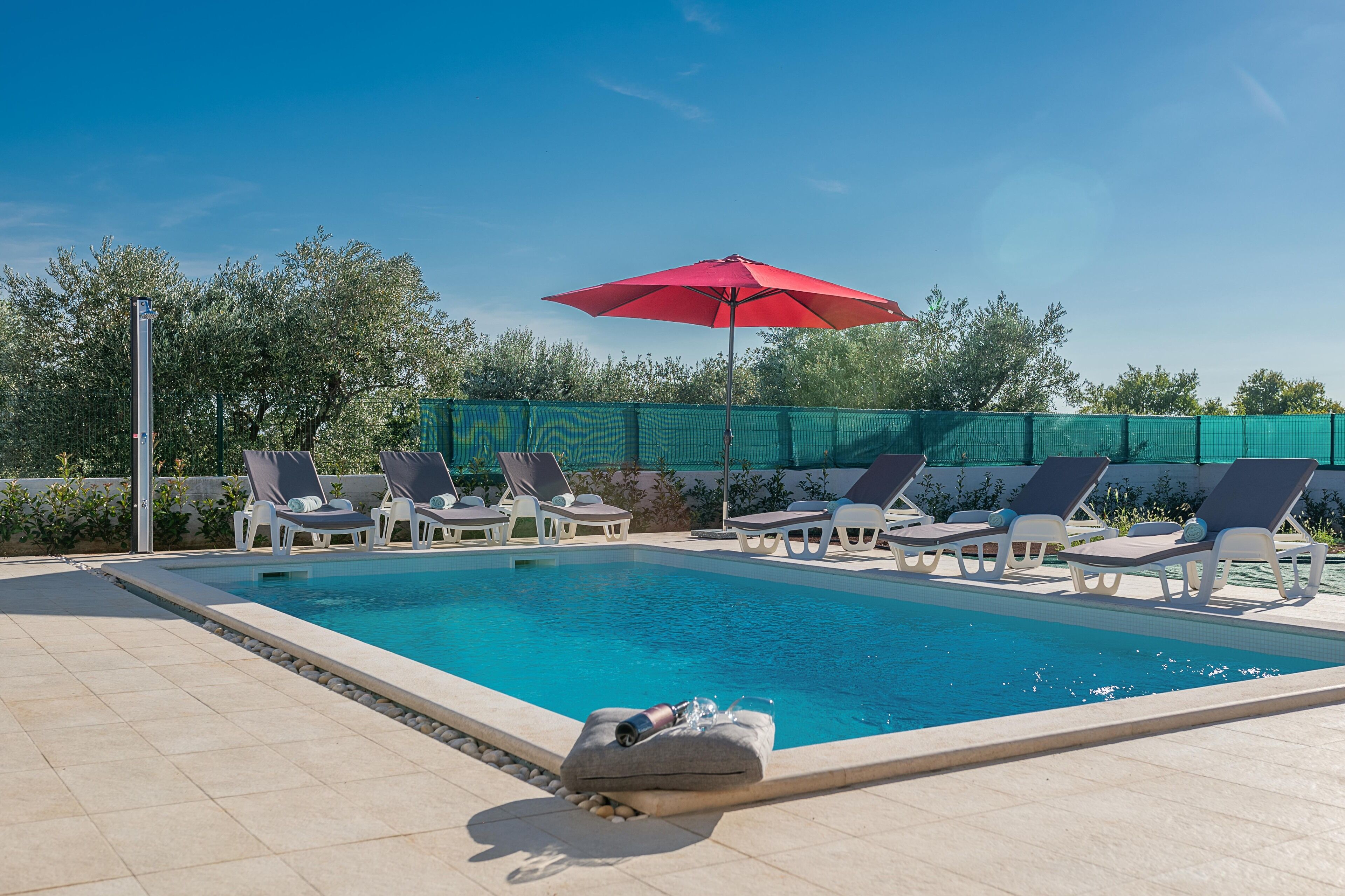 A swimming pool with lounge chairs and a red umbrella.