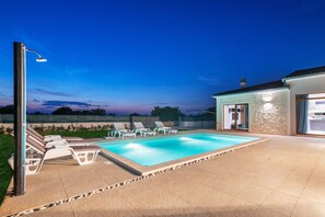 Une piscine avec des chaises longues, un patio couvert et un mur en pierre.