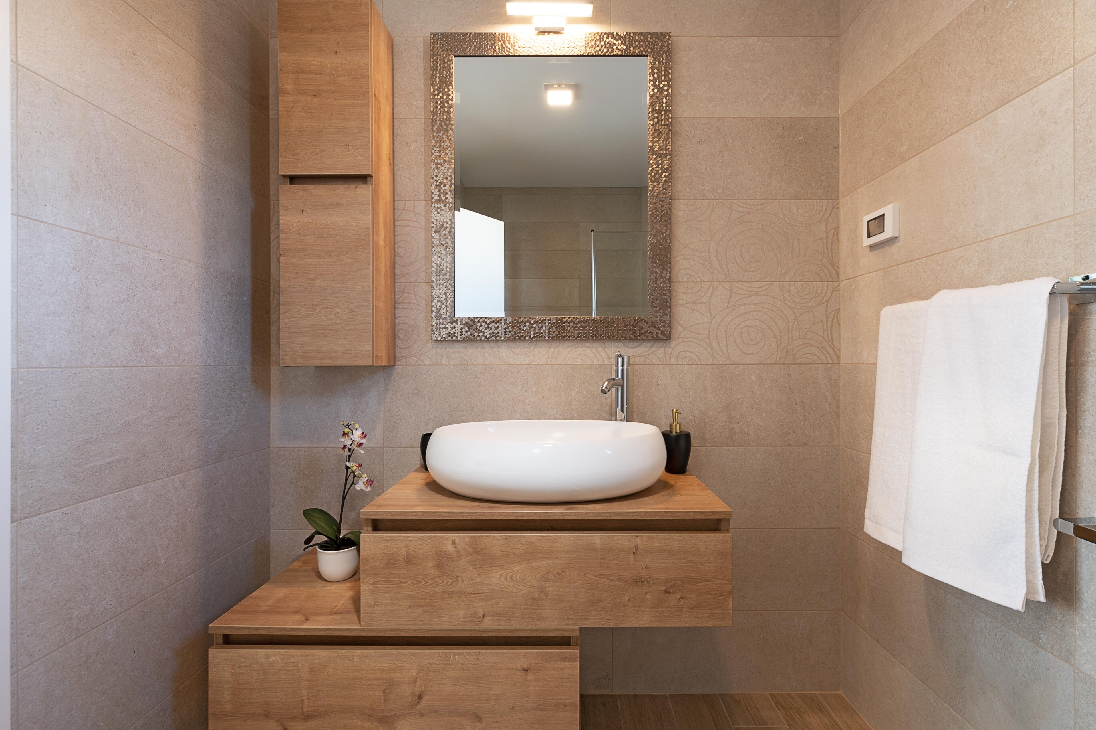 A modern bathroom with a wooden vanity, a white sink, and a large mirror.